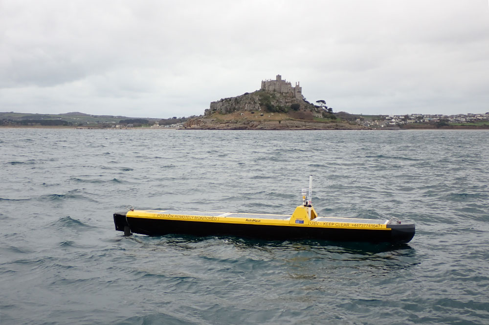 Yellow AutoNaut autonomous vessel at sea with St Michael's Mount in the background